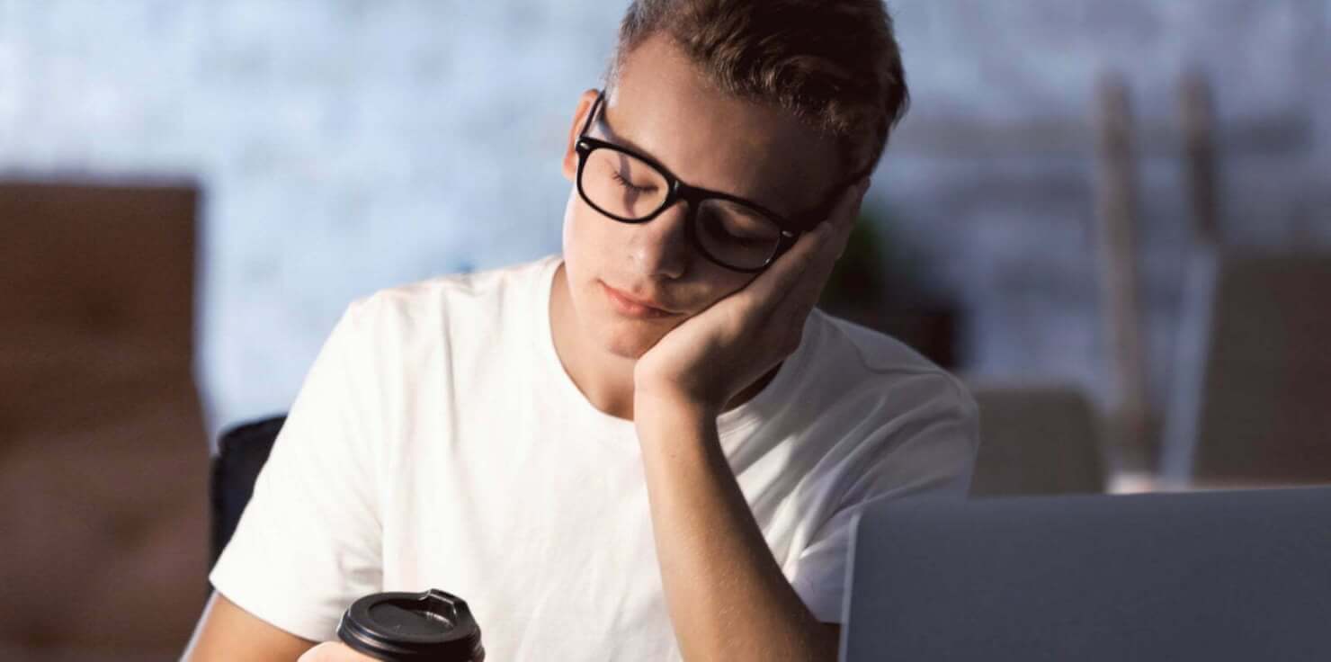 A young man sitting at his desk in an addiction recovery center with a cup of coffee.