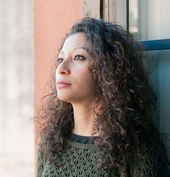 A woman with curly hair is leaning against a window in an addiction recovery center.