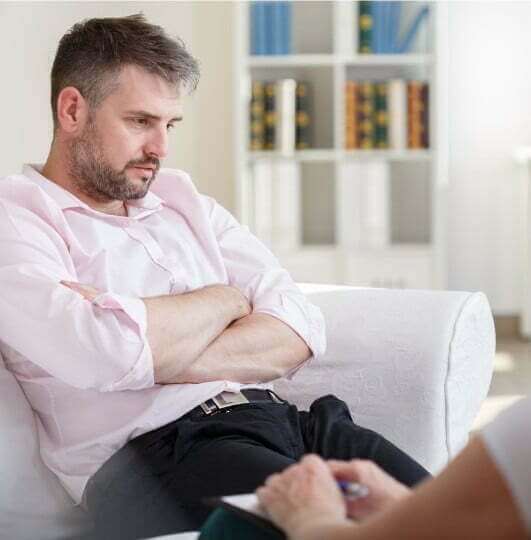 A man sitting on a couch talking to a therapist in an outpatient program.