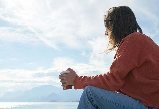 A woman sitting on a rock enjoying a cup of coffee during her outpatient program.