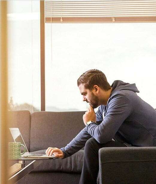 A man participating in a men's only rehab program while sitting on a couch and looking at his laptop.
