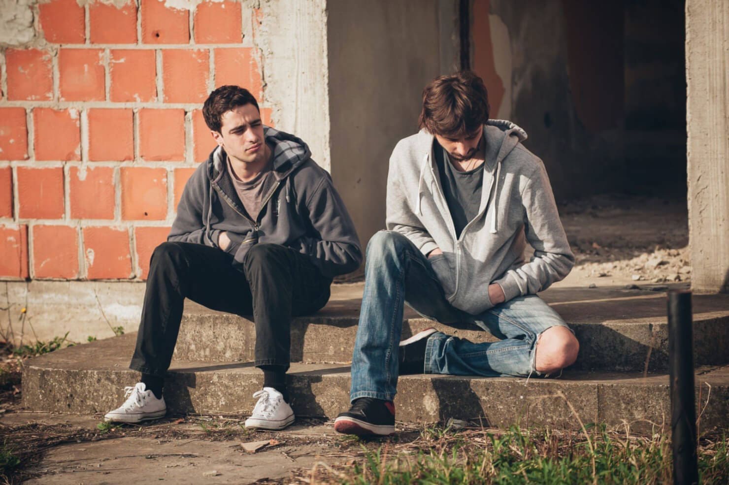 Two men sitting against a brick wall
