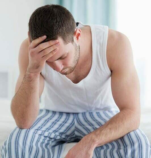 A man in a tank top is drowsy and hunched over.