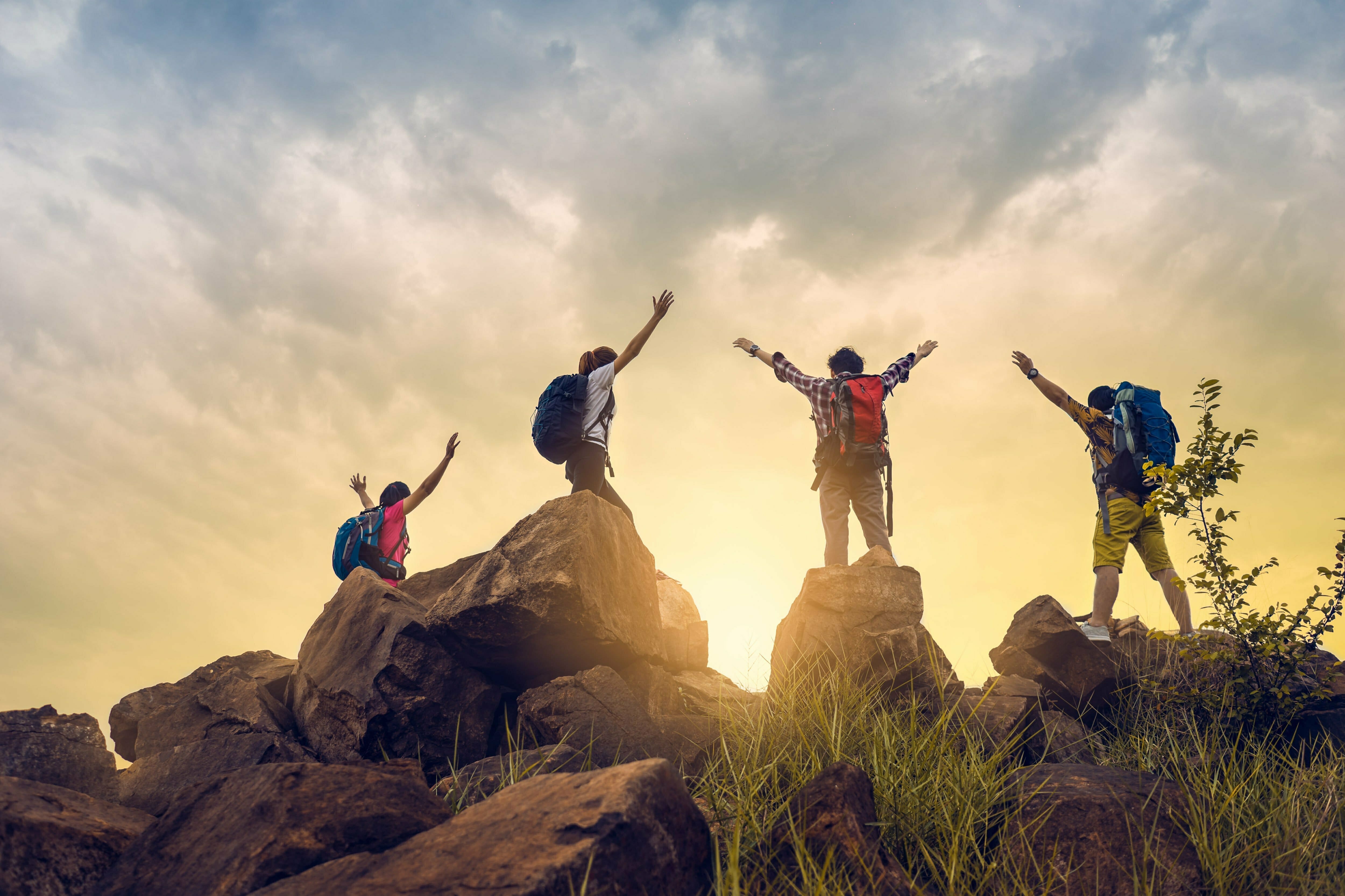 A group of hikers standing on top of a rock during their rehab journey, with their arms raised in celebration.