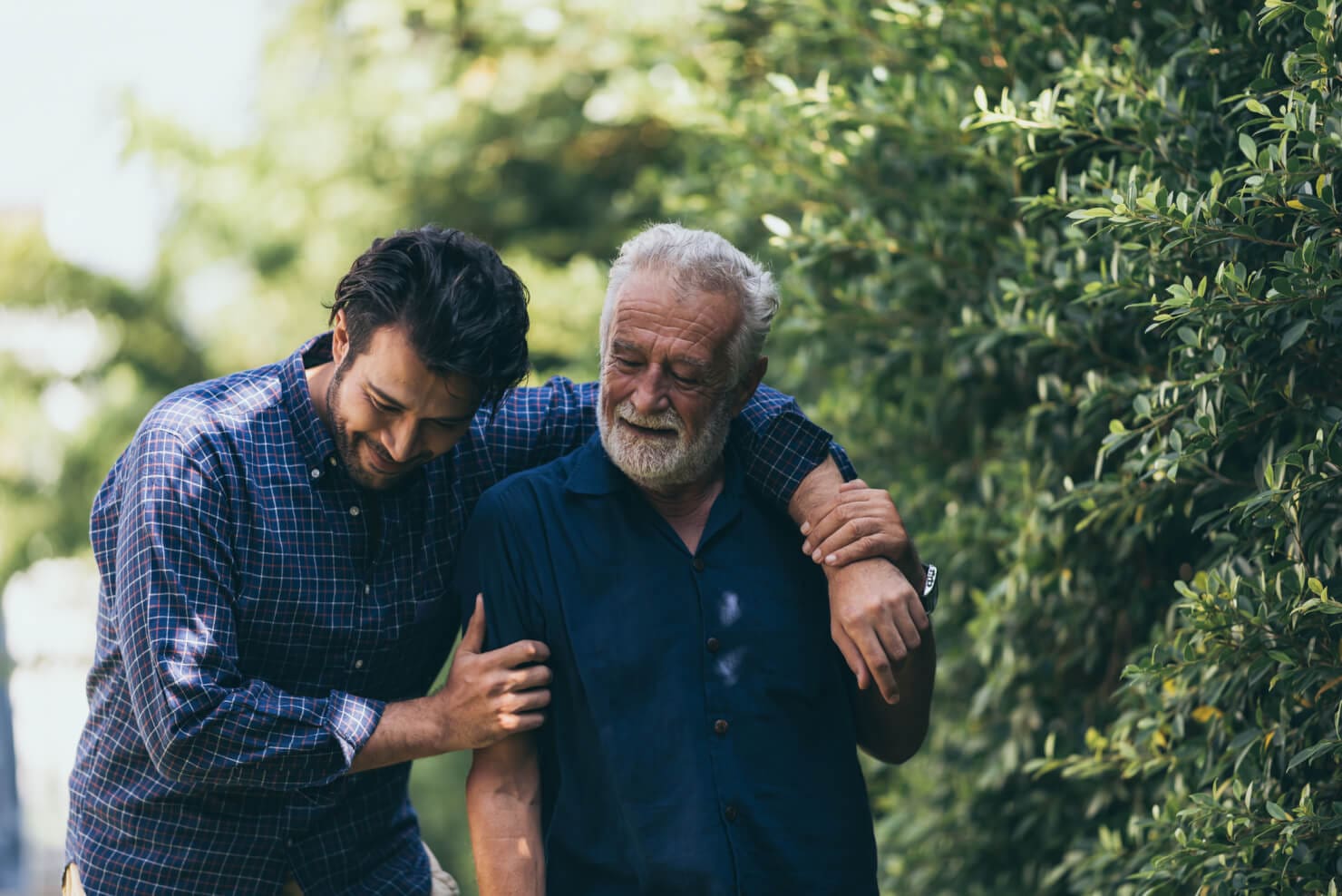 Two older men embracing each other in a park near an addiction recovery center.