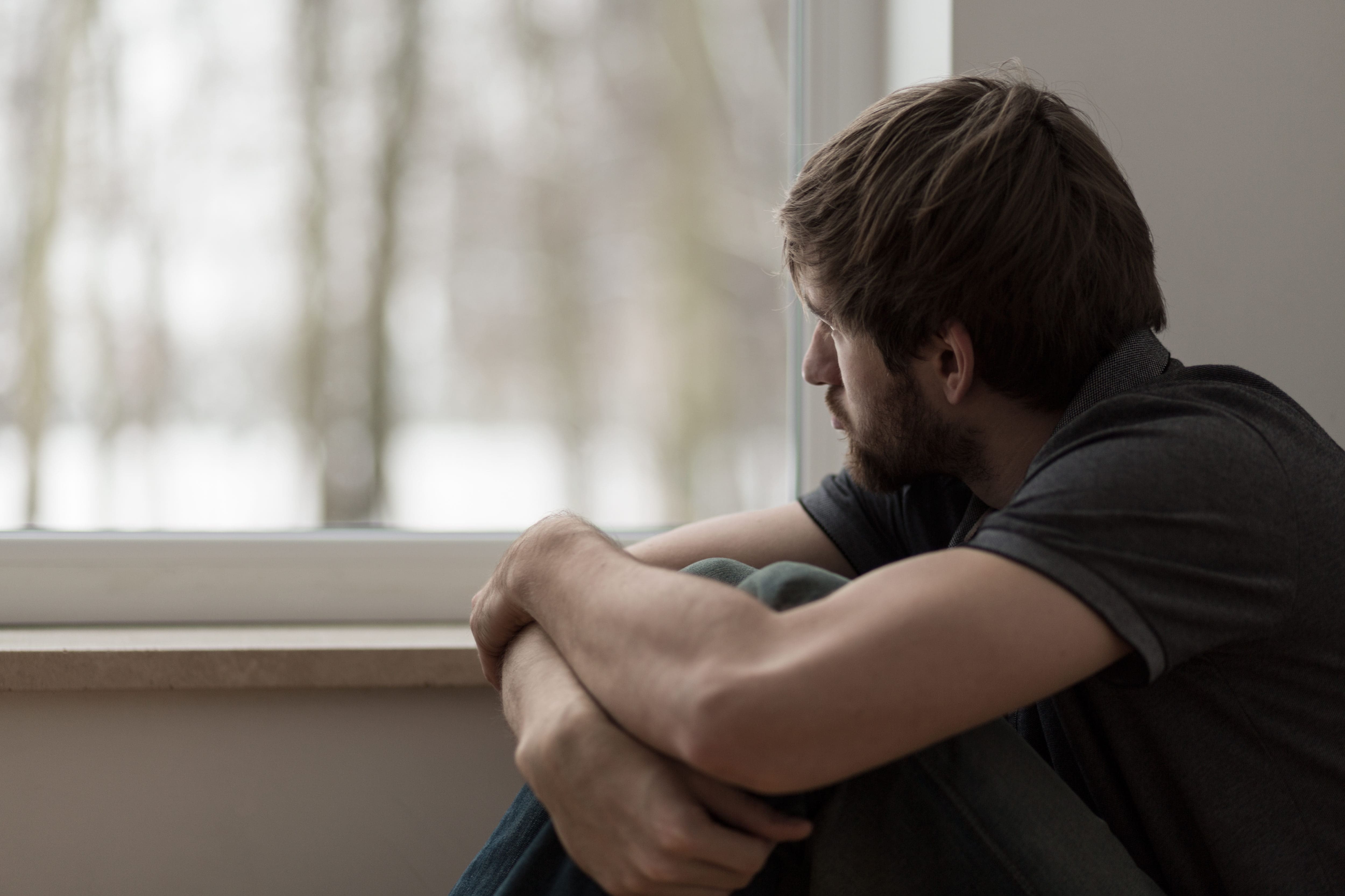 A man sitting in front of a window at a men's only rehab center, looking out.