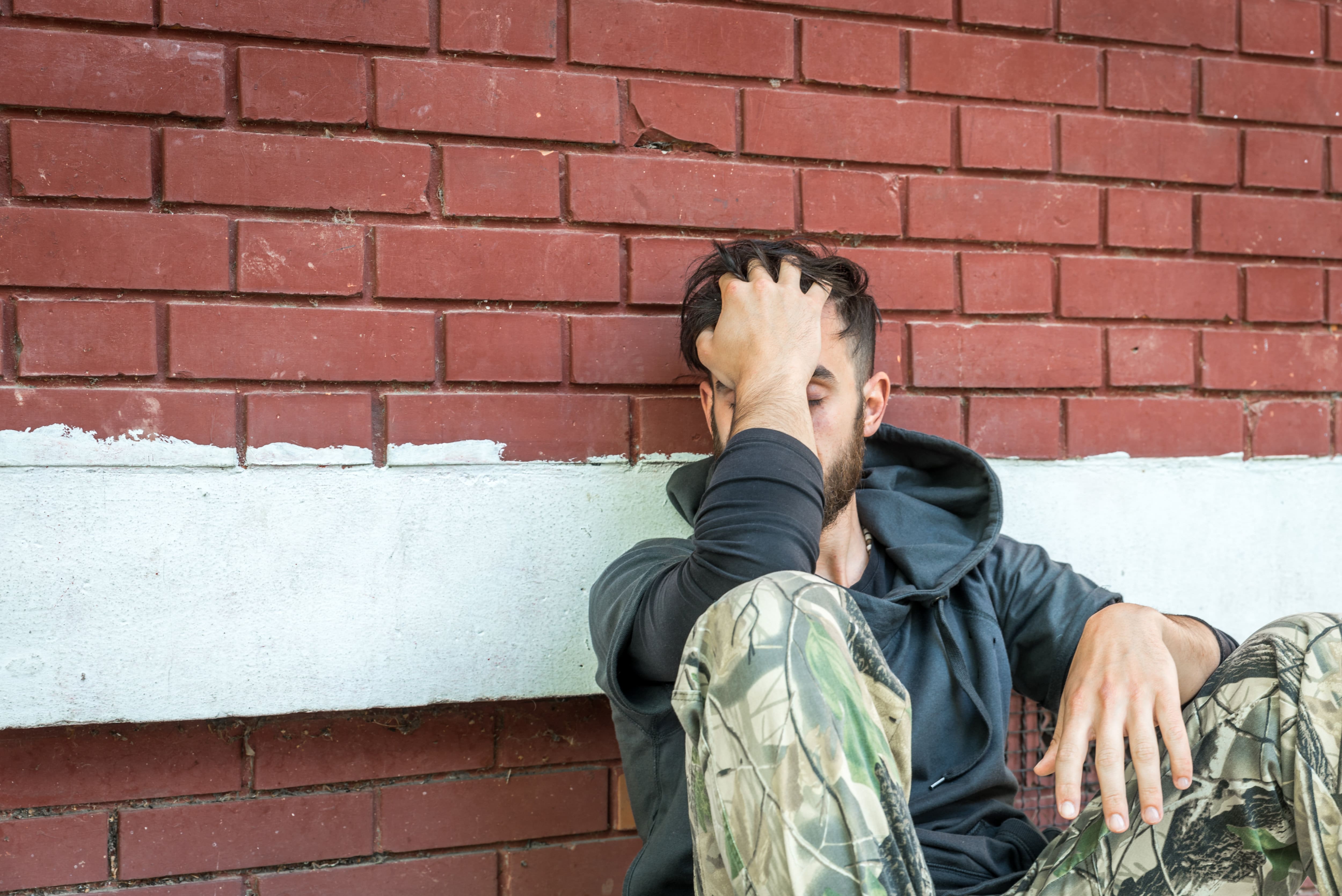 A man sitting on a brick wall at an addiction recovery center, with his hand on his face.