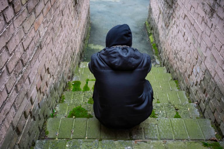 A man in a black hoodie sitting on a set of stairs at an addiction recovery center.