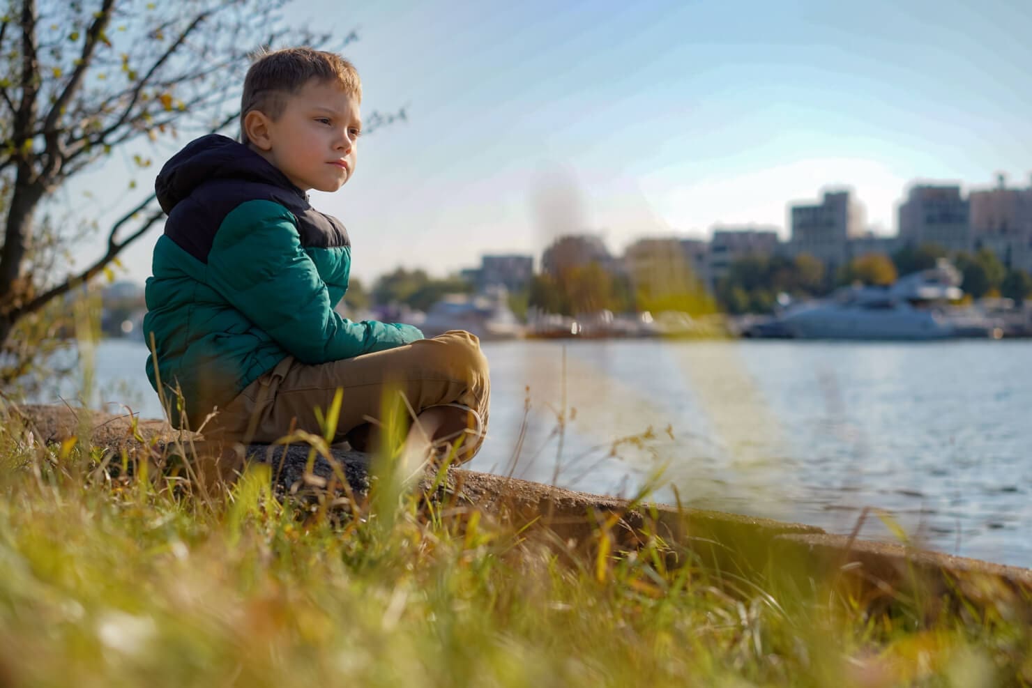 A young boy peacefully sitting on the shore of a lake.
