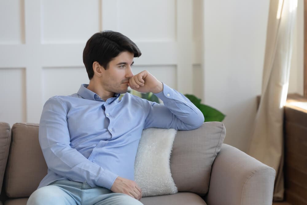 A man sitting on a couch at a men's only rehab, looking at his phone.