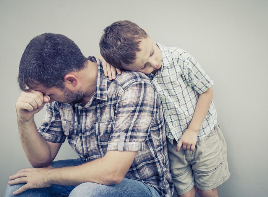 A man and his son are sitting on a gray background in an outpatient program or drug detox center.