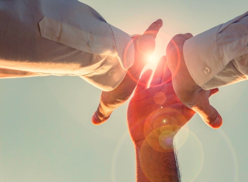 Two hands reaching for each other with the sun behind them, symbolizing the hopeful journey of addiction recovery in an inpatient treatment center.