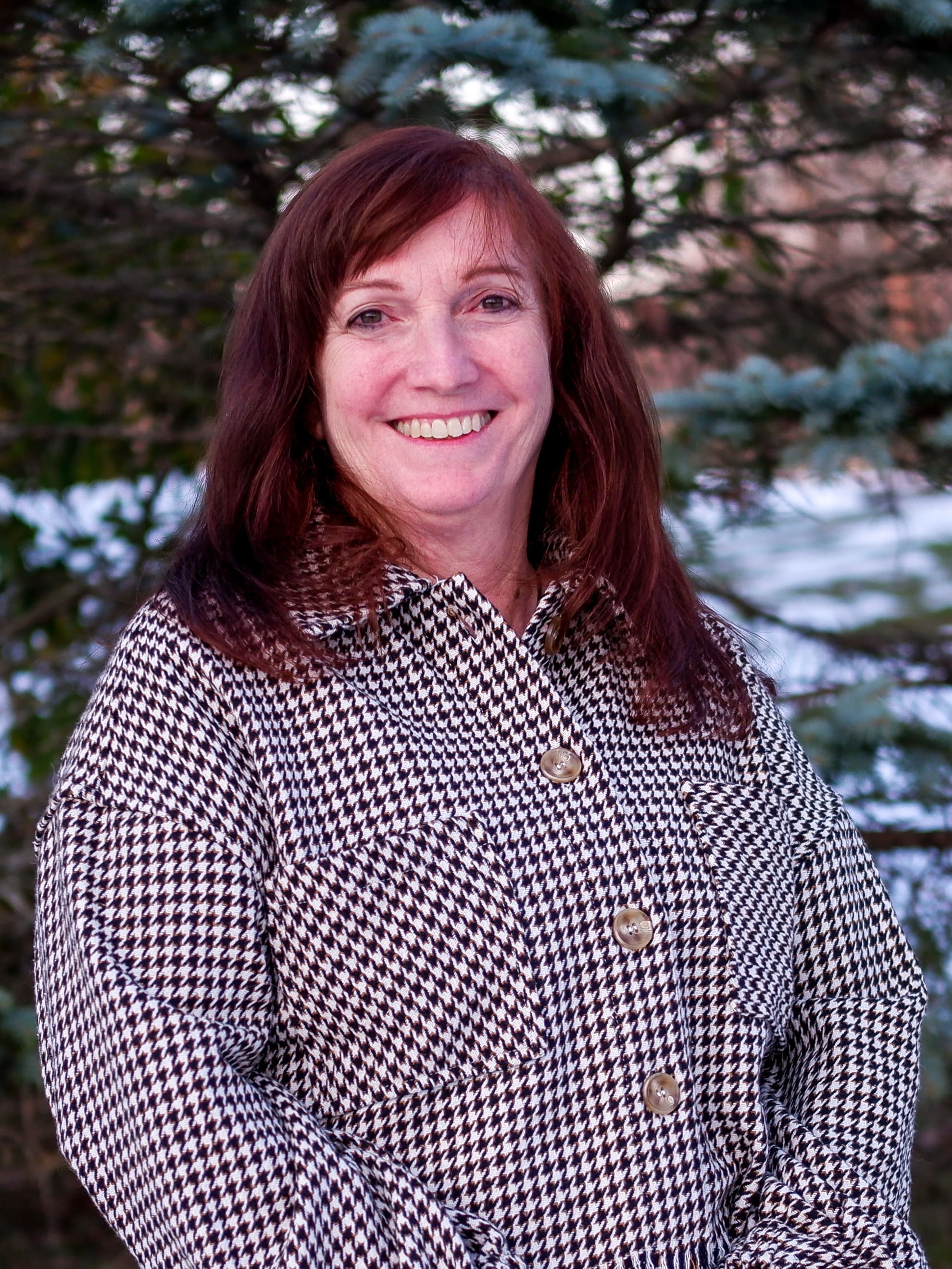 A woman in a plaid shirt smiling in front of trees at an addiction recovery center.