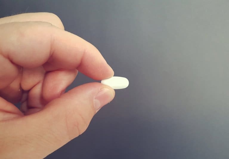 A person's hand holding a white pill at an addiction recovery center.