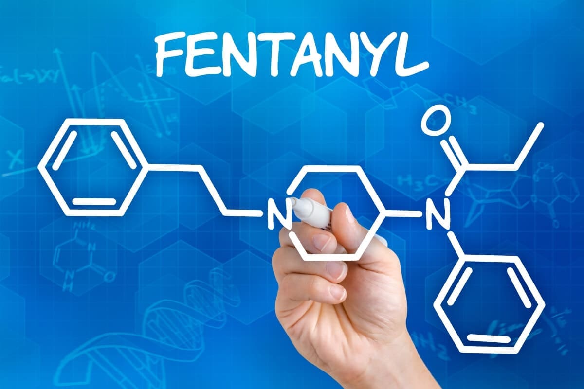 A hand drawing the word fentanyl on a blue background in an addiction recovery center.