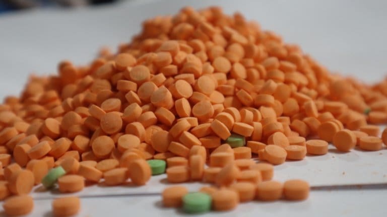 A pile of orange and green pills on a white surface at an addiction recovery center.