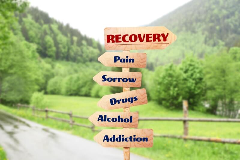 A sign advertising an addiction recovery center, offering rehab and outpatient programs for individuals struggling with pain, sorrow, drugs, and addiction.
