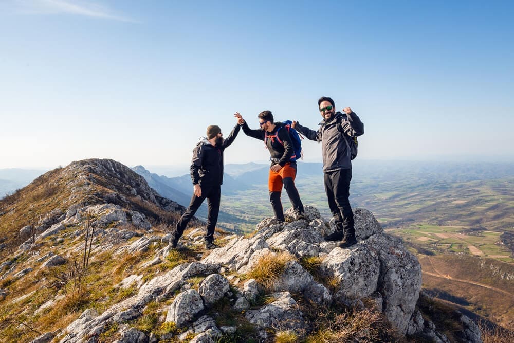 Three hikers standing on top of a mountain, enjoying their journey in the great outdoors.