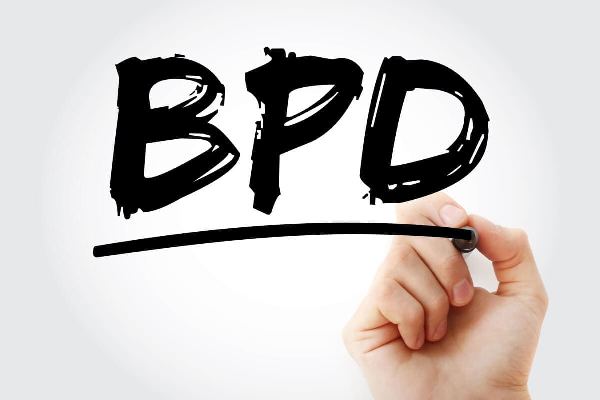 A hand writing the word "bpd" on a transparent screen in an outpatient program.
