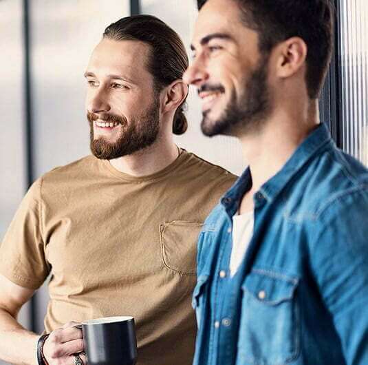 Two smiling men in a Cleveland, OH drug-alcohol rehab looking out a window, one holding a coffee mug.