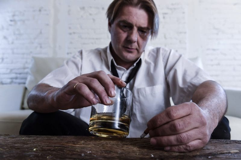 A man is holding a glass of whiskey inpatient treatment.